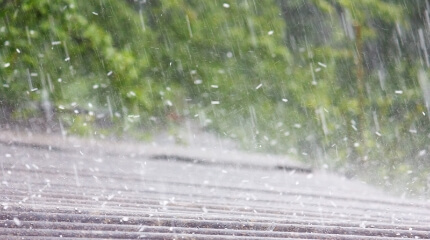 工場・倉庫の劣化したスレート屋根の雨漏りを補修し断熱効果もある防水工事リリーフ工法（カバー工法）を施工することで遮音性の向上につながることを表す雨に打たれる屋根